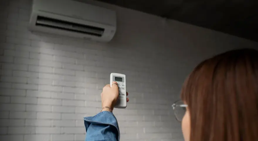 Persona ajusta control remoto de aire acondicionado, pensando en el consumo de la bomba de calor.