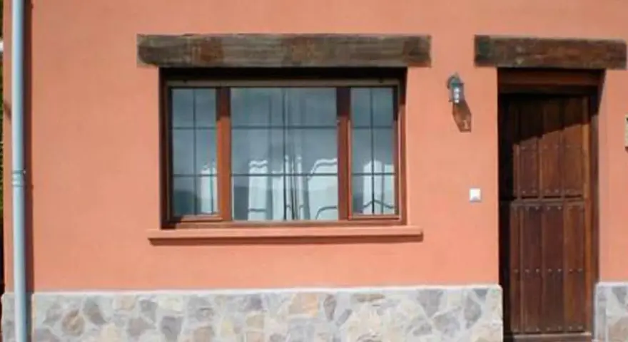 Fachada con zócalo de piedra irregular, ventana de madera y puerta rústica. Muestra distintos tipos de zócalos para paredes exteriores.