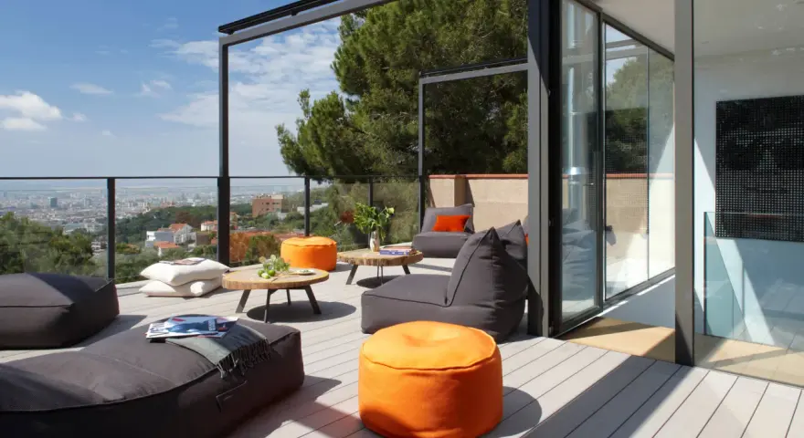 Cómoda terraza ático con sillones y pufs naranjas, vistas a la ciudad y un gran pino.