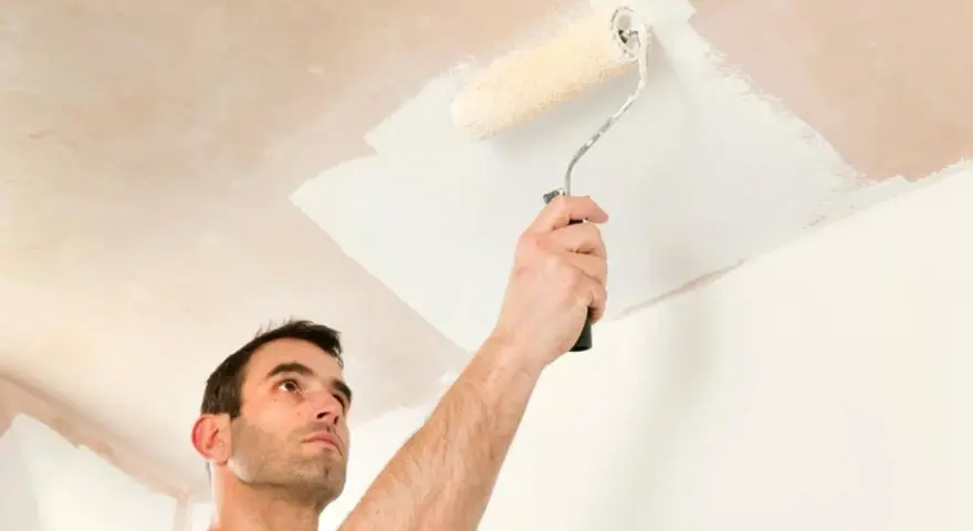 Hombre pintando el techo con rodillo. La pregunta de si que se pinta primero el techo o las paredes es clave para un buen acabado.