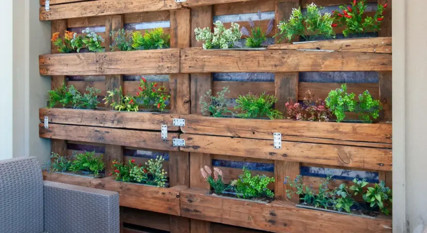 Jardineras con palets crean un jardín vertical lleno de plantas verdes y flores de colores, un oasis en el balcón.