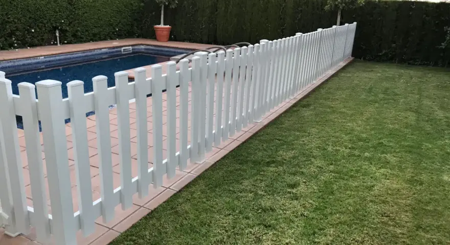 Una verja de jardín blanca protege una piscina y un césped verde.