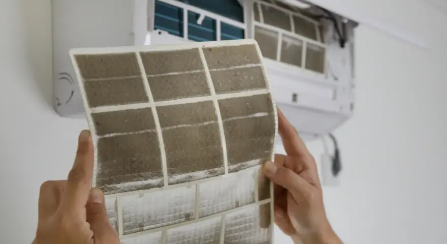Manos sostienen un filtro de aire acondicionado sucio, mostrando cómo cambiarlo para un aire más limpio.