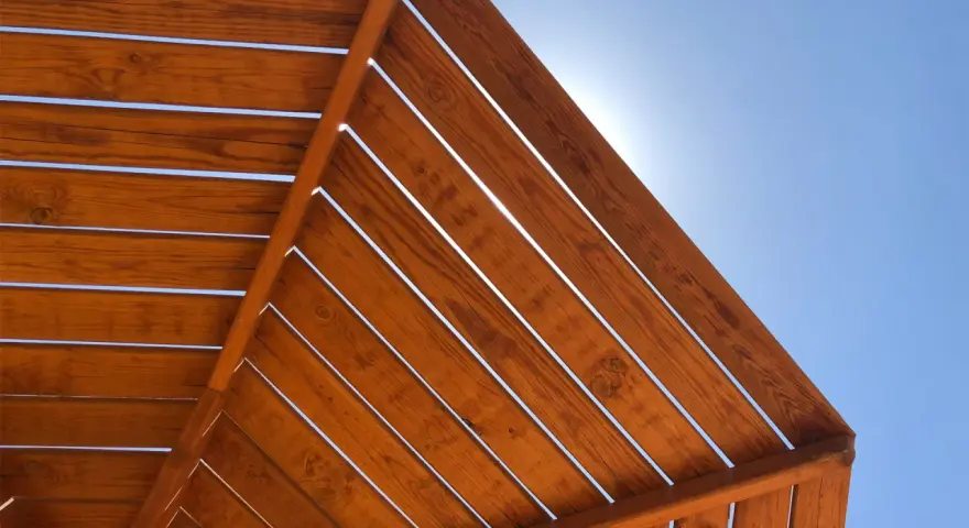 Estructura de madera con tratamiento para exterior, con lamas de madera barnizada bajo un cielo azul brillante.