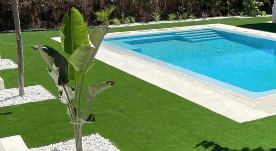 Jardín moderno con piscina y césped artificial. La colocación de césped artificial realza la belleza del espacio.