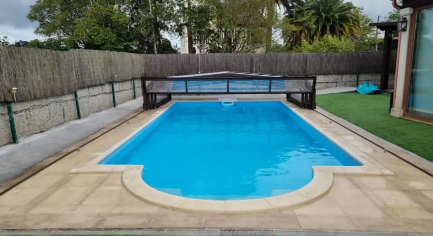 Piscina con cubierta retráctil, rodeada de césped artificial y un sistema para canalizar agua de lluvia.