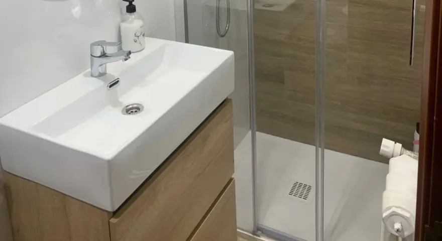 Lavabo moderno con mueble de madera y ducha acristalada. Un ejemplo de cuartos de baño modernos y funcionales.
