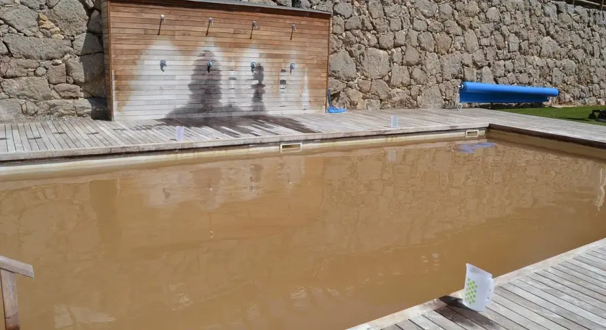 Una piscina de agua salada con un revestimiento de madera y duchas. El agua es de color marrón turbio.