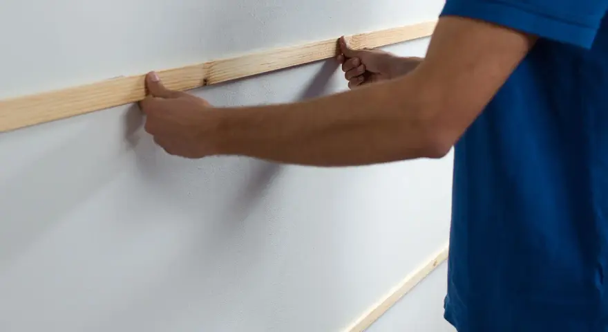Man placing wooden slats on a white wall, demonstrating como poner listones de madera en la pared.