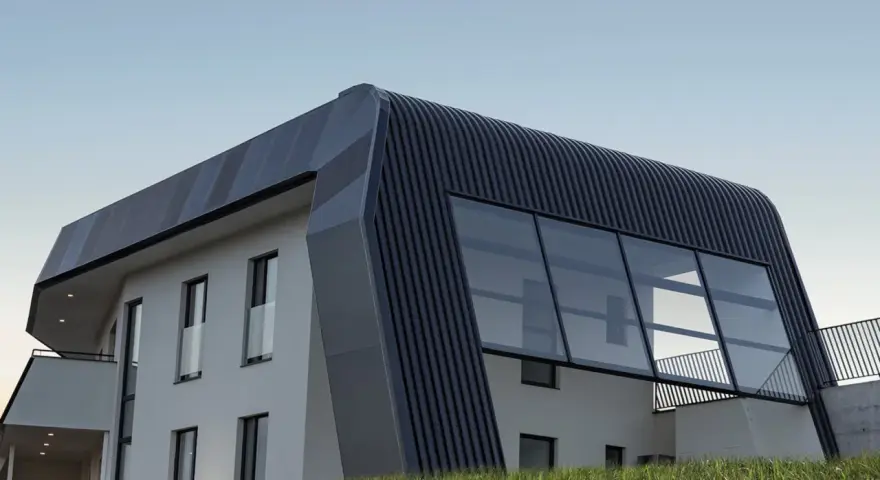 Moderna casa autosuficiente con techo curvo y grandes ventanales, rodeada de hierba alta bajo un cielo despejado.