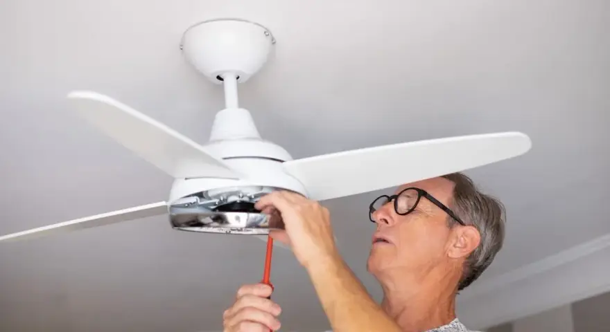Hombre con gafas ajusta un ventilador de techo pladur con un destornillador.