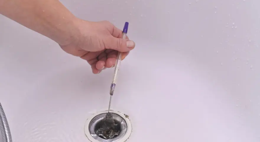 Mano usando un bolígrafo para quitar pelo y desatascar la ducha.
