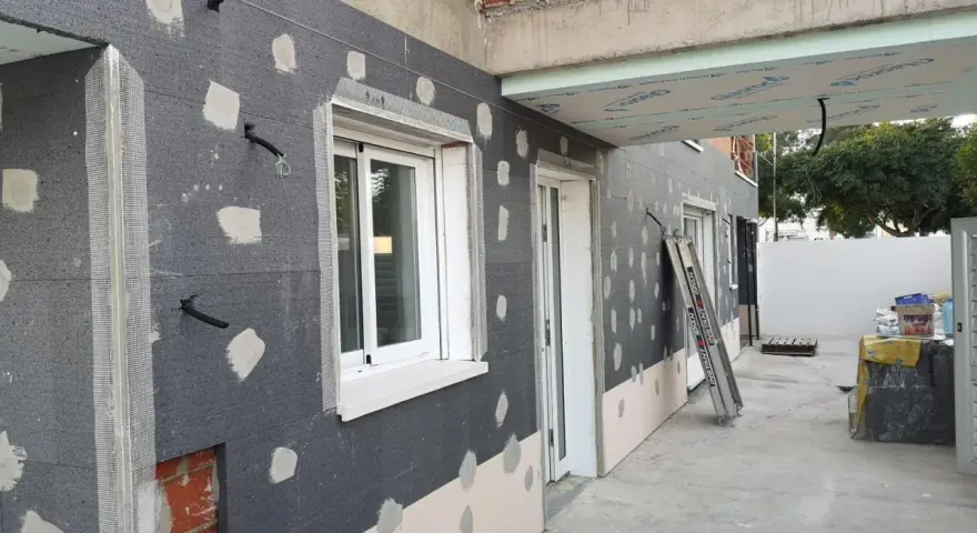 Fachada en construcción con aislamiento SATE, tuberías y ventanas.