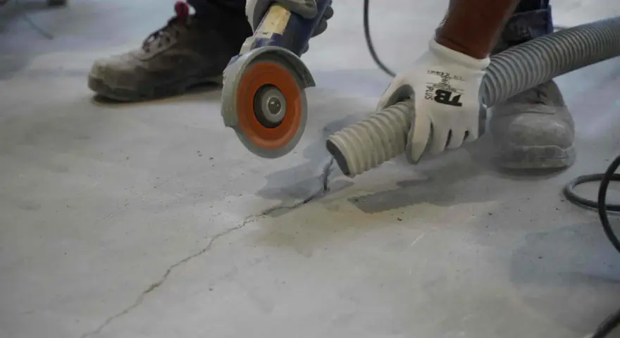 Trabajador usa una amoladora para hacer una solera de hormigón sobre tierra, aspirando el polvo.