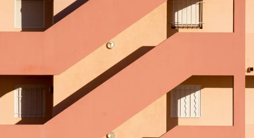 Fachada con escaleras y ventanas, sombras marcadas. Un ejemplo de cómo impermeabilizar pared exterior para protegerla.