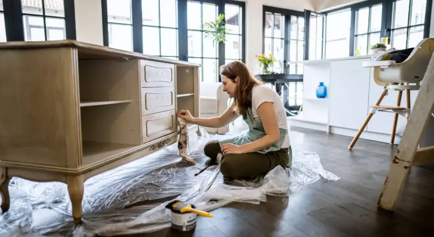 Mujer aplicando una capa de pintura a un mueble antiguo.