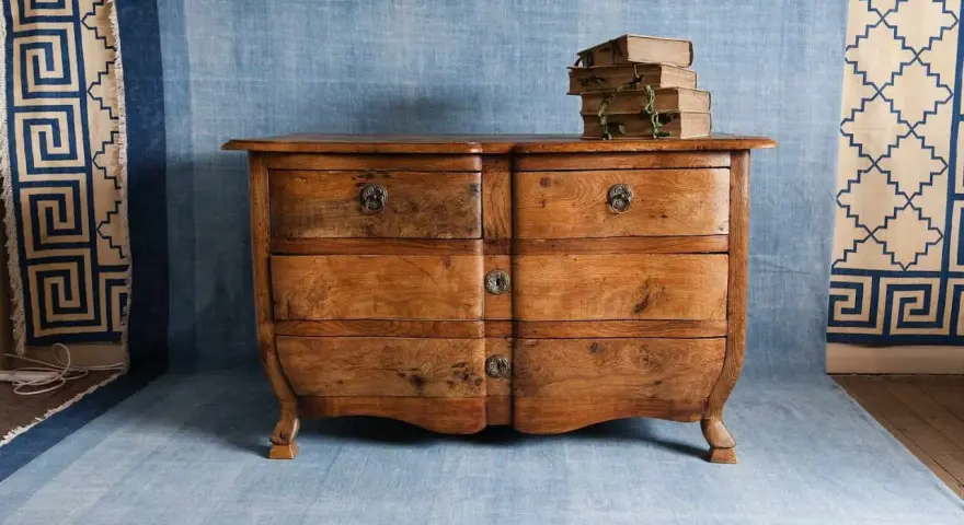 Cómoda de madera antigua, lista para pintar. Unos libros apilados descansan sobre ella.