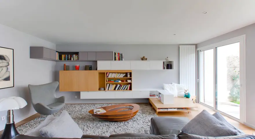 Salón moderno con estanterías empotradas y una **color crema pared**. Sofá de cuero, sillón gris y mesa de centro ovalada.