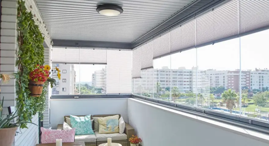 Ideas para tapar balcón: un espacio acogedor con sofá, plantas y vistas urbanas.