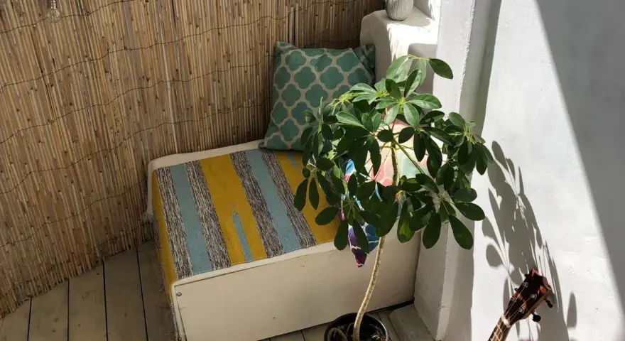 Un rincón acogedor para decorar balcon. Un banco con cojines, planta y luces crea un ambiente relajado.