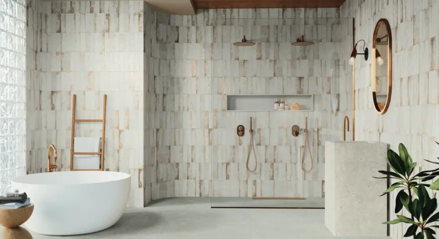 Baño moderno con bañera exenta y ducha doble. Las paredes presentan azulejos con un diseño rústico y detalles dorados, reflejando las últimas tendencias azulejos baño.