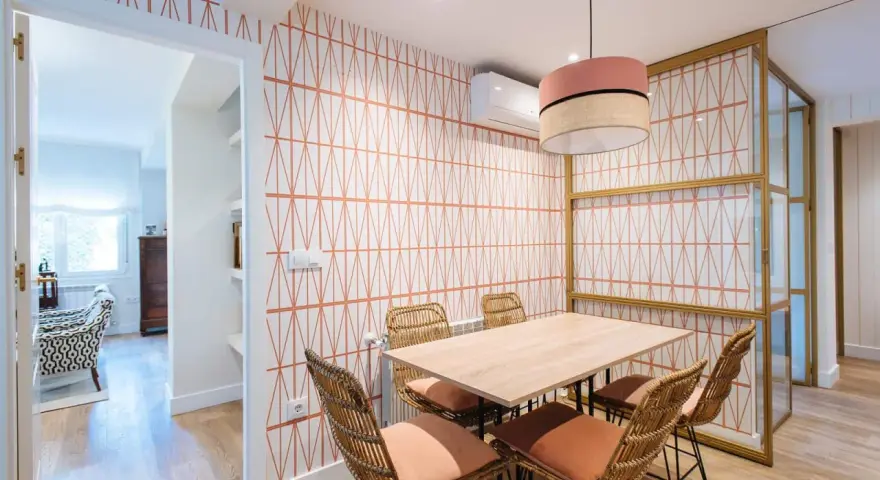 Comedor con pared empapelada con un diseño geométrico en naranja. Mesa de madera con sillas de ratán y cojines terracota.