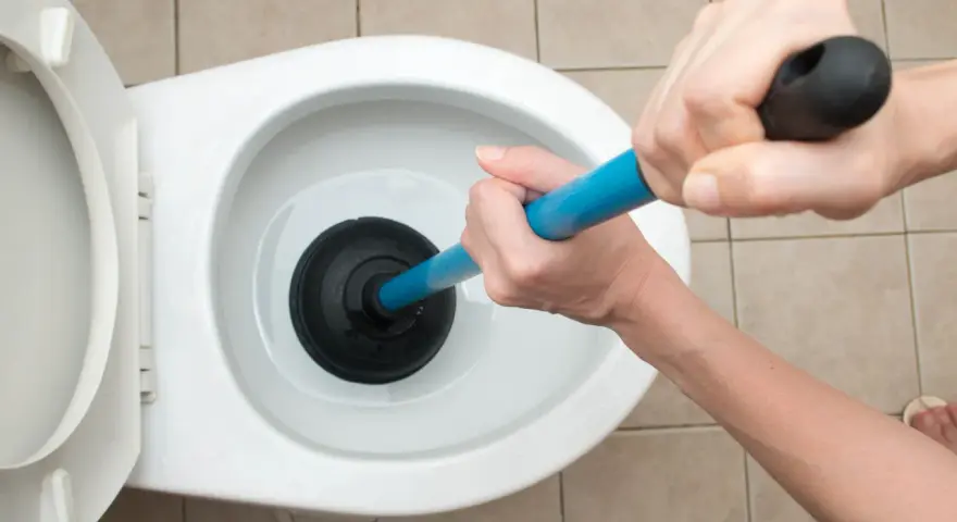 Manos usando un desatascador para como desatascar un water.