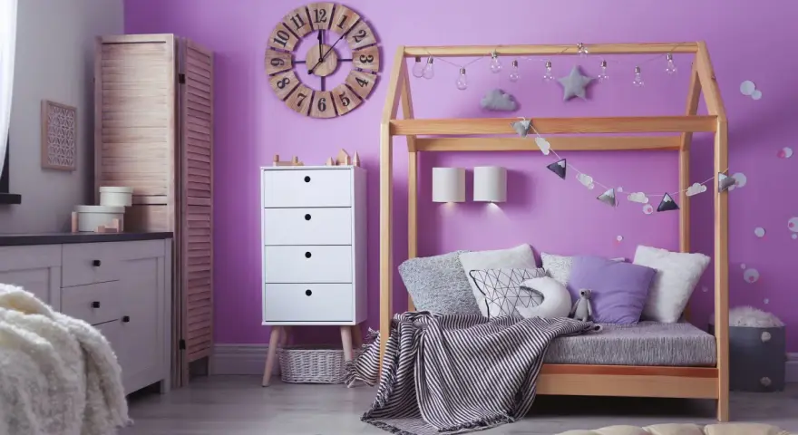 Adolescentes pintan habitación juvenil. Un espacio lleno de color lila, con cama de madera, cómoda blanca y decoración infantil.