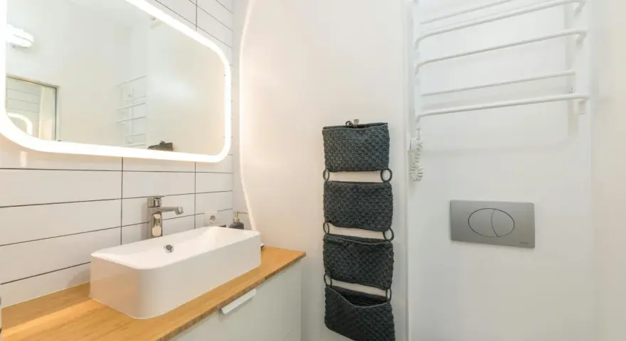 Moderno baño pequeño con lavabo sobre encimera de madera, espejo iluminado y organizadores de pared. ¡Una reforma de baño pequeño funcional y estilosa!