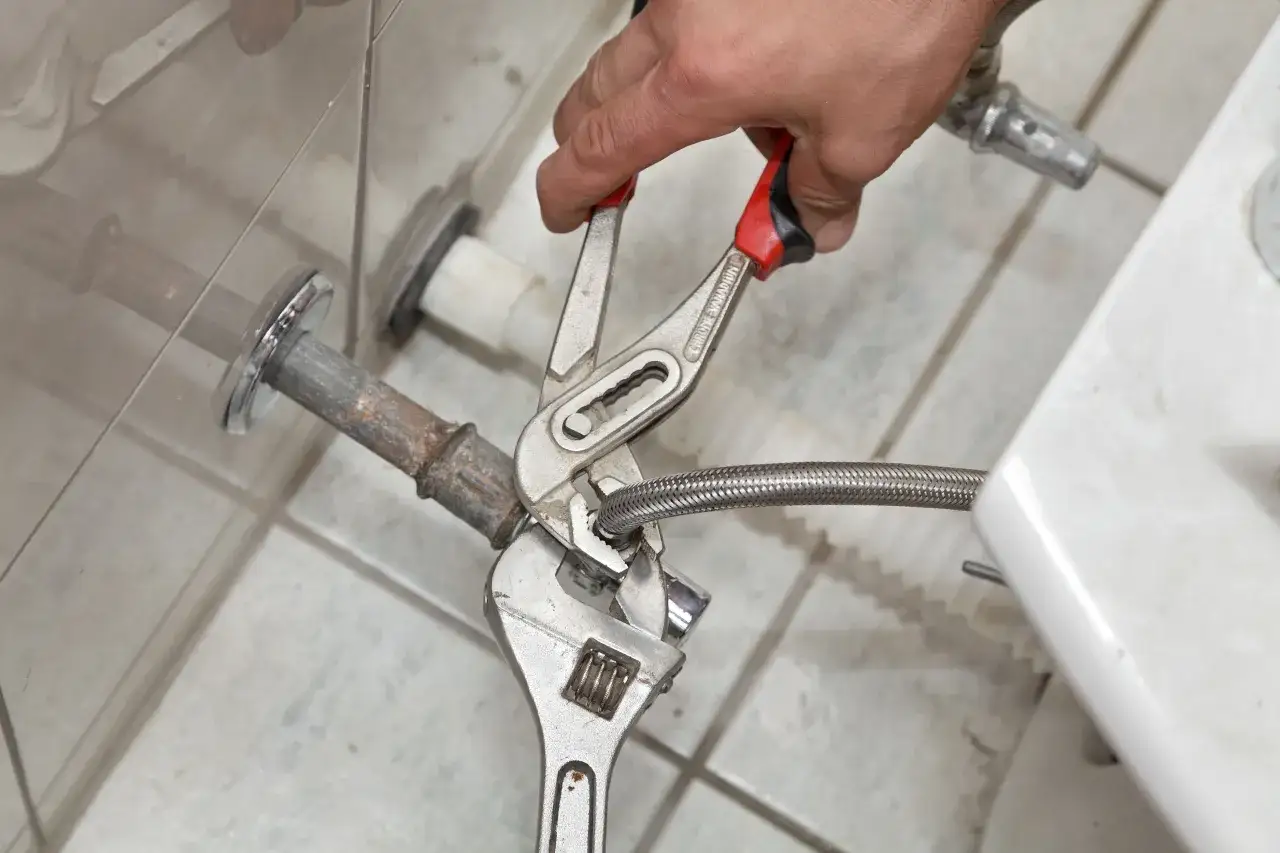 Mano con llave inglesa y alicates desconectando la manguera de agua para como quitar un bidet.