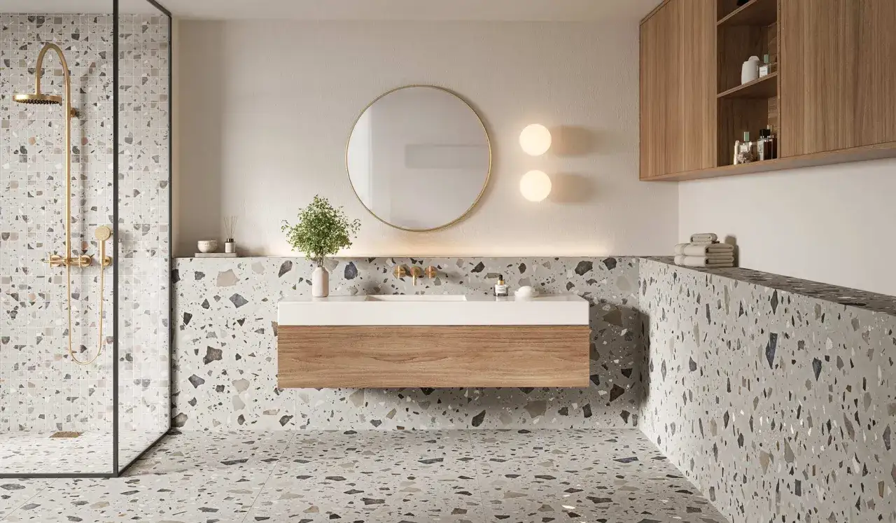 Ba&ntilde;o moderno con azulejos de terrazo, reflejando las &uacute;ltimas tendencias azulejos ba&ntilde;o. Ducha dorada, lavabo flotante y espejo redondo.