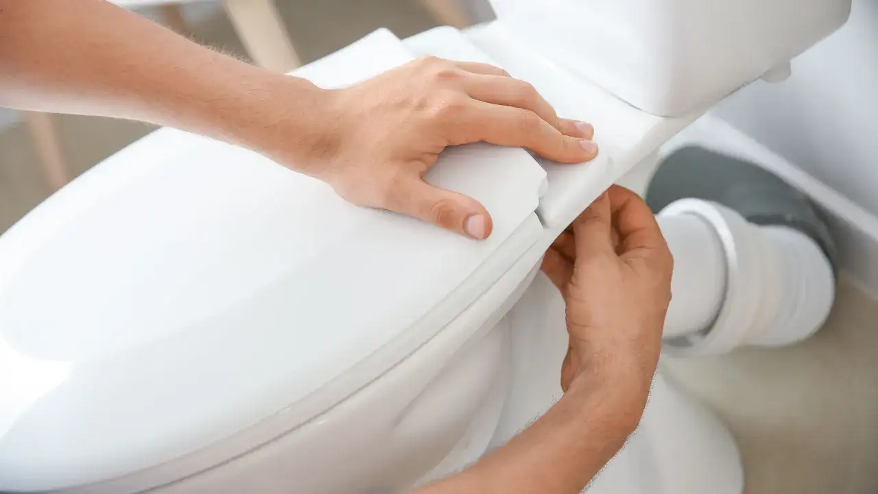 Man's hands carefully fitting the toilet seat, part of the process to como instalar un inodoro al suelo.