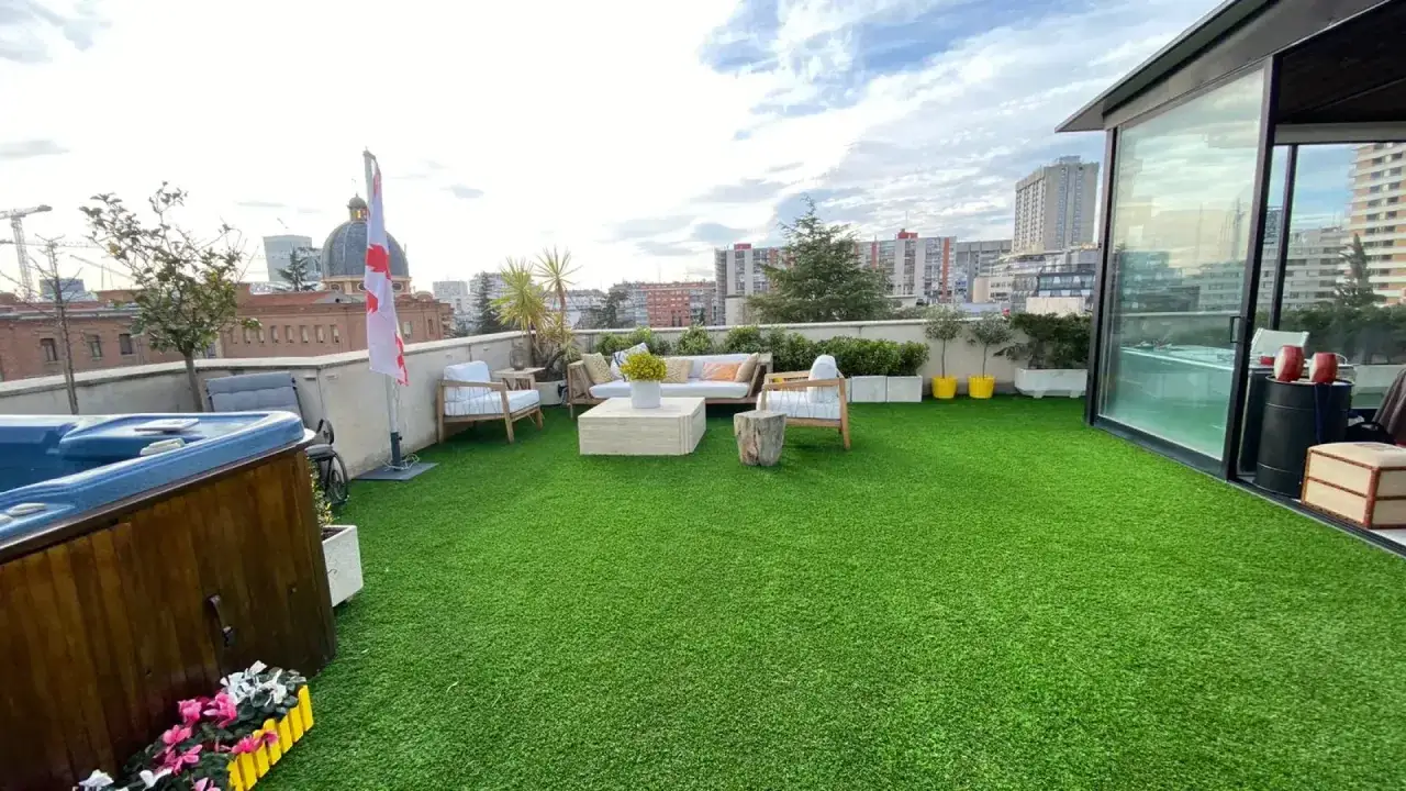 Terraza con jacuzzi y mobiliario de exterior sobre c&eacute;sped artificial. Un espacio ideal para poner c&eacute;sped artificial en terraza y disfrutar del sol.