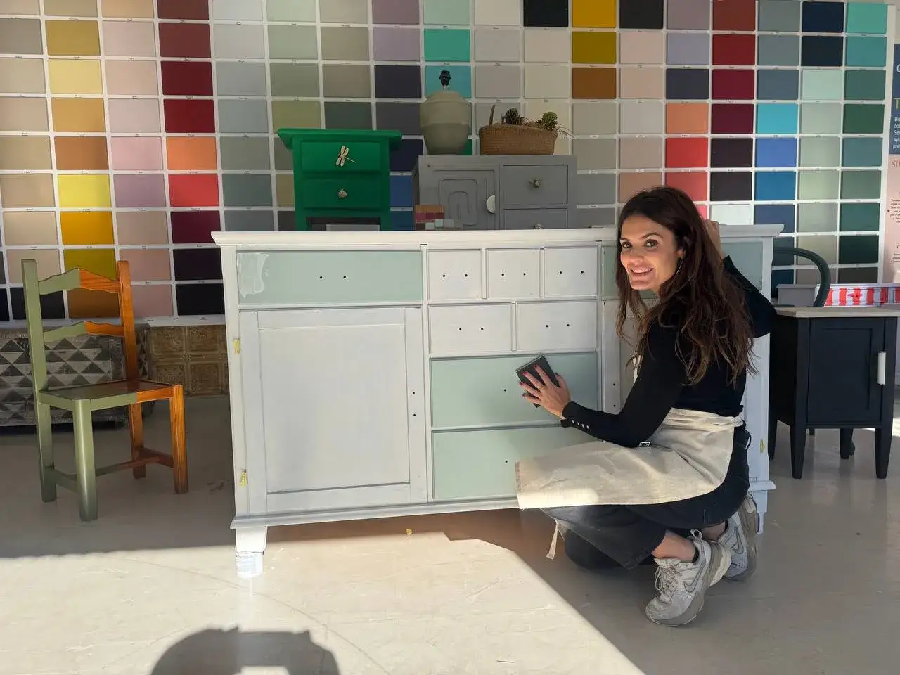 Mujer sonr&iacute;e mientras trabaja en un mueble, demostrando c&oacute;mo pintar muebles de madera sin lijar.