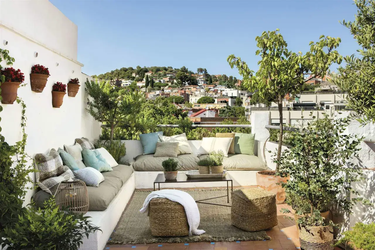 Un rincón perfecto para chill out en la terraza, con cómodos cojines, plantas y vistas a la ciudad.