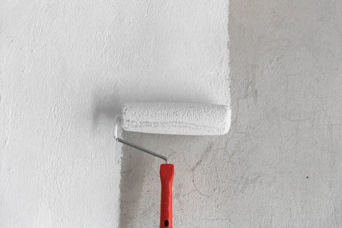 Rodillo aplicando pintura mineral blanca sobre una pared texturizada gris.