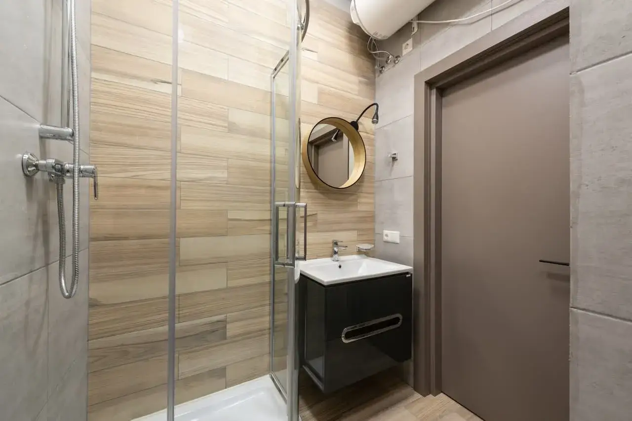 Moderno baño pequeño con ducha de cristal, lavabo flotante y espejo redondo. Una reforma funcional y elegante.