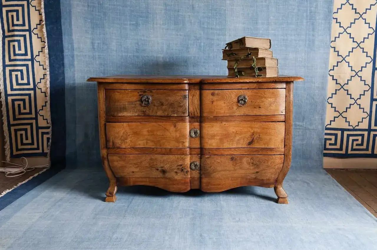 C&oacute;moda de madera antigua con seis cajones, lista para pintar. Apilado de libros antiguos sobre ella.