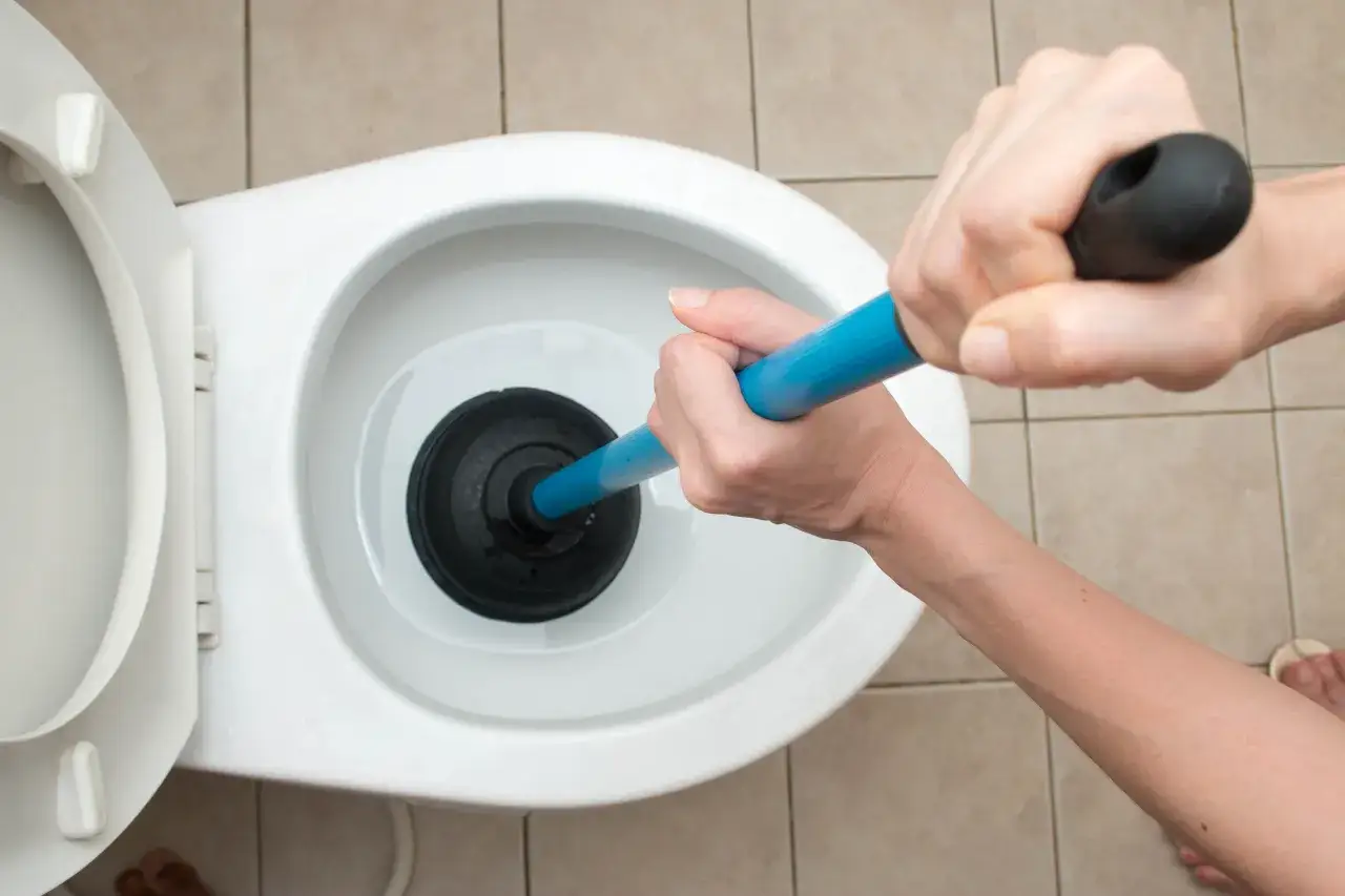 Manos usando un desatascador para como desatascar un water.