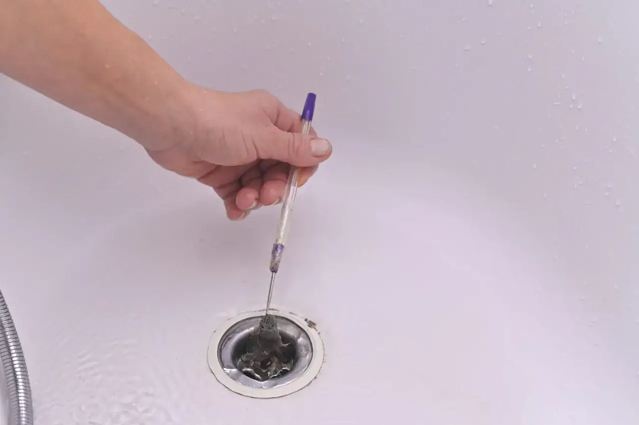 Mano usando un bol&iacute;grafo para quitar pelos y desatascar la ducha.