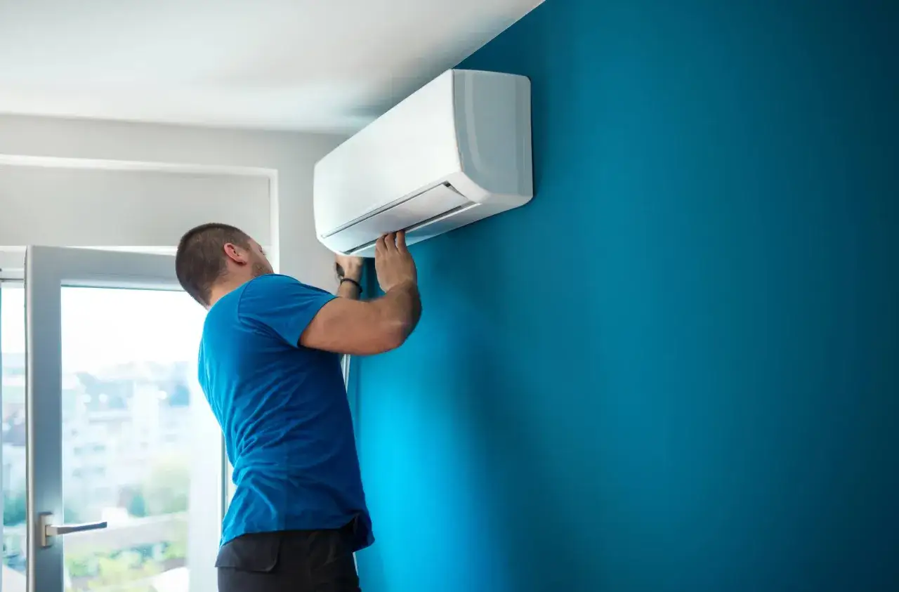 T&eacute;cnico instalando un aire acondicionado en una pared azul. Gu&iacute;a visual para como instalar un aire acondicionado.