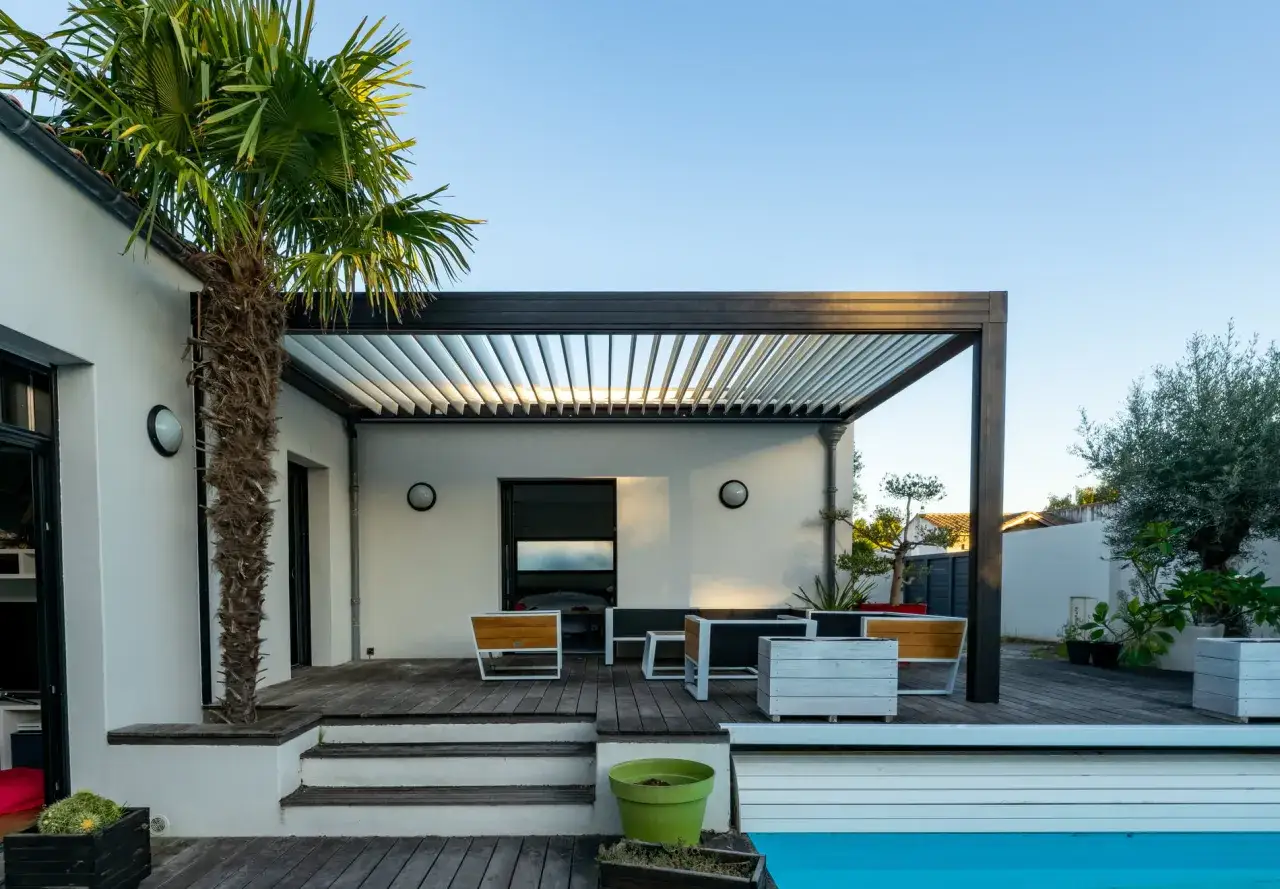 Terraza con piscina y una moderna pergola bioclimatica. Muebles de exterior y palmera.