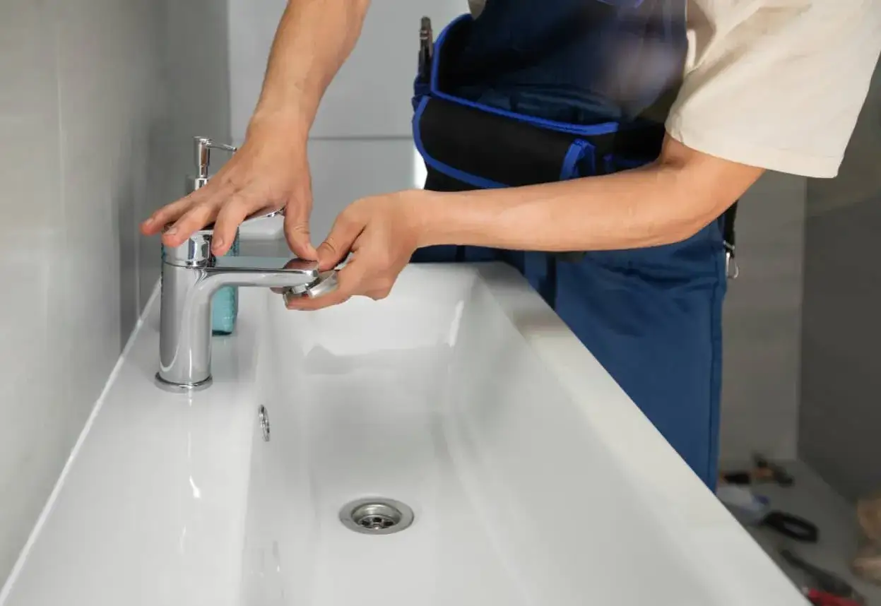Man con mono azul trabajando en el lavabo, listo para cambiar grifo lavabo.