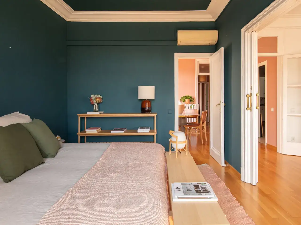 Habitación con paredes azul oscuro y techo blanco. La cama tiene mantas rosas y verdes. Se ve un comedor al fondo. ¿Qué se pinta primero el techo o las paredes?