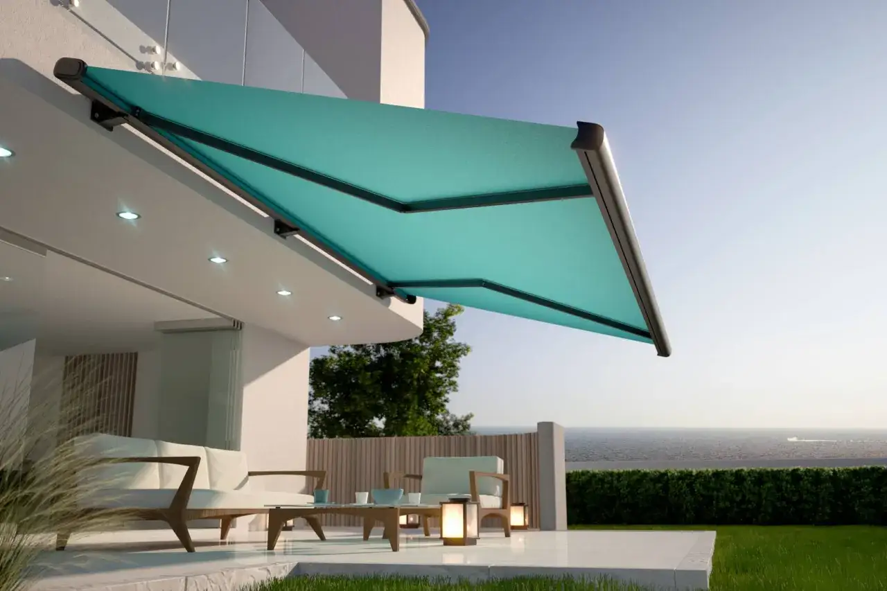 Toldo moderno de color turquesa, uno de los colores de toldos de moda, protege un &aacute;rea de descanso exterior con vistas al mar.