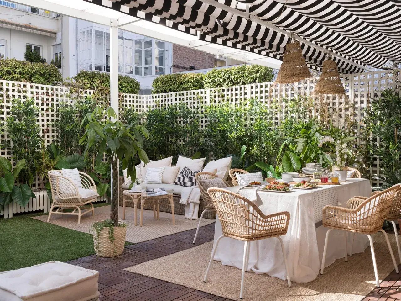 Terraza con muebles de rat&aacute;n y vegetaci&oacute;n exuberante, ideal para como tapar la vista del vecino. Mesa puesta para comer al aire libre.