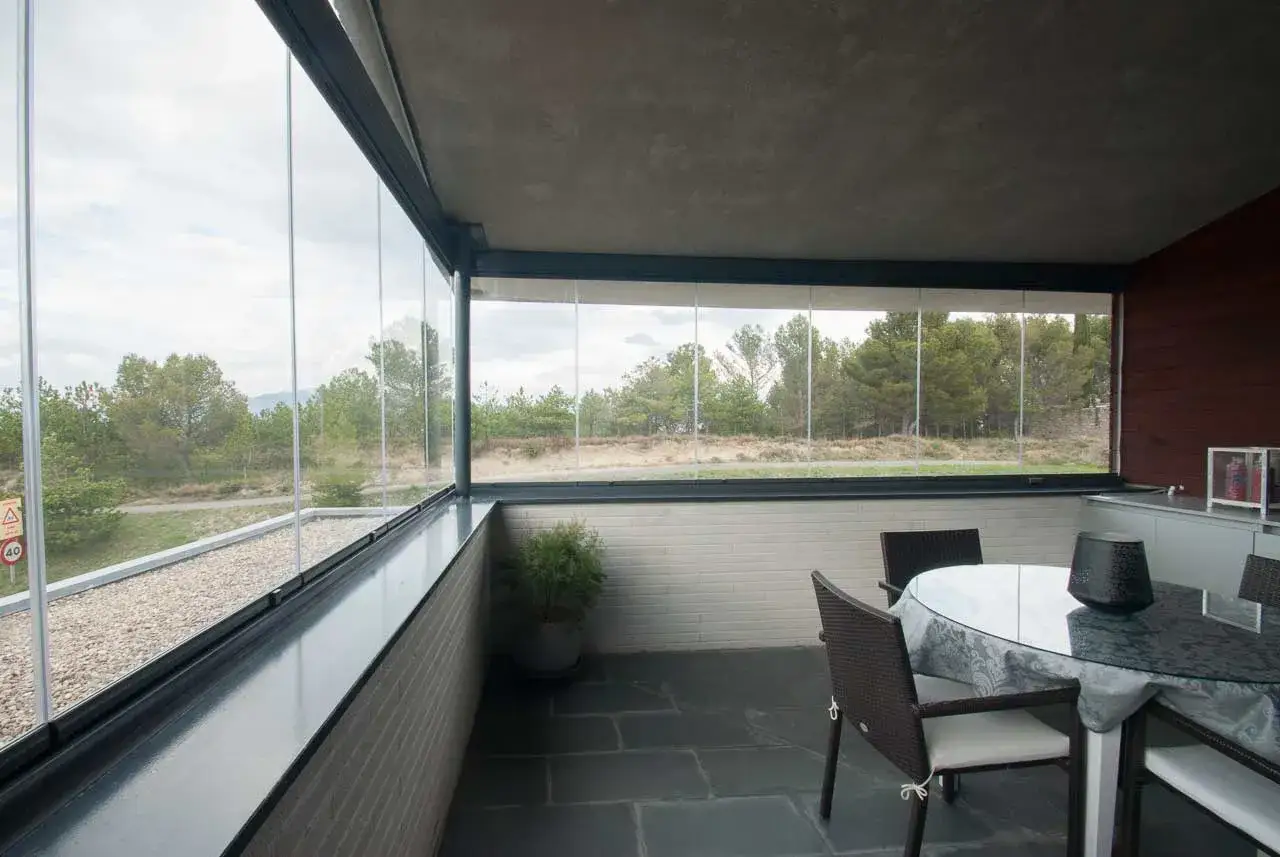 Terraza acristalada con mesa y sillas, ideal para cerrar el espacio y disfrutar del paisaje boscoso.
