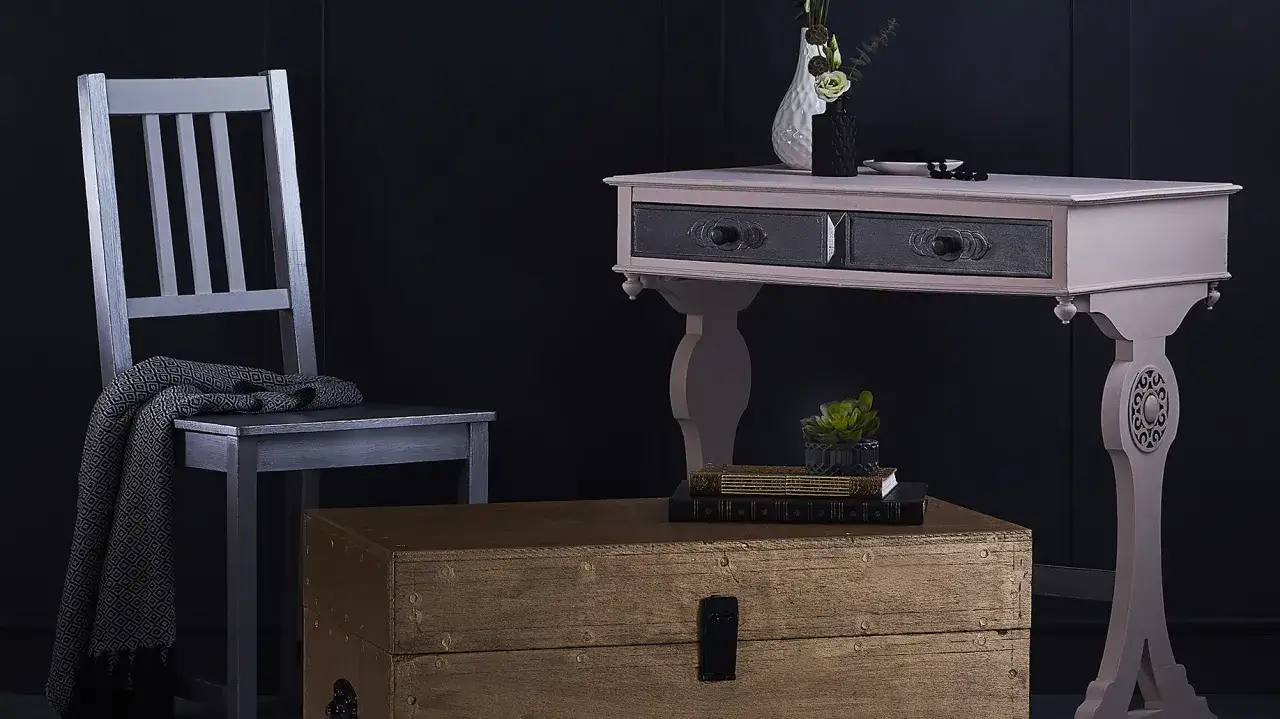 Silla plateada y cómoda con cajones oscuros, un baúl de madera y un jarrón. Ideas para saber como lacar un mueble y darle un nuevo look.