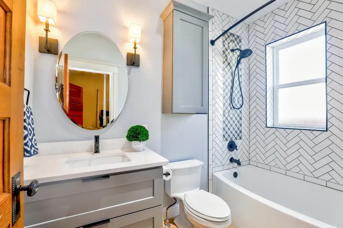 Baño moderno con lavabo, inodoro y bañera. La fontanería negra y las baldosas en espiga añaden estilo. La altura de las medidas de fontanería del baño es estándar.
