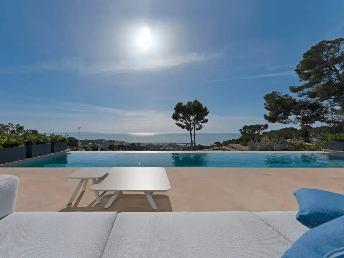 Una espectacular piscina desbordante con vistas al mar. El sol brilla en un cielo azul claro, creando un ambiente de vacaciones perfecto.